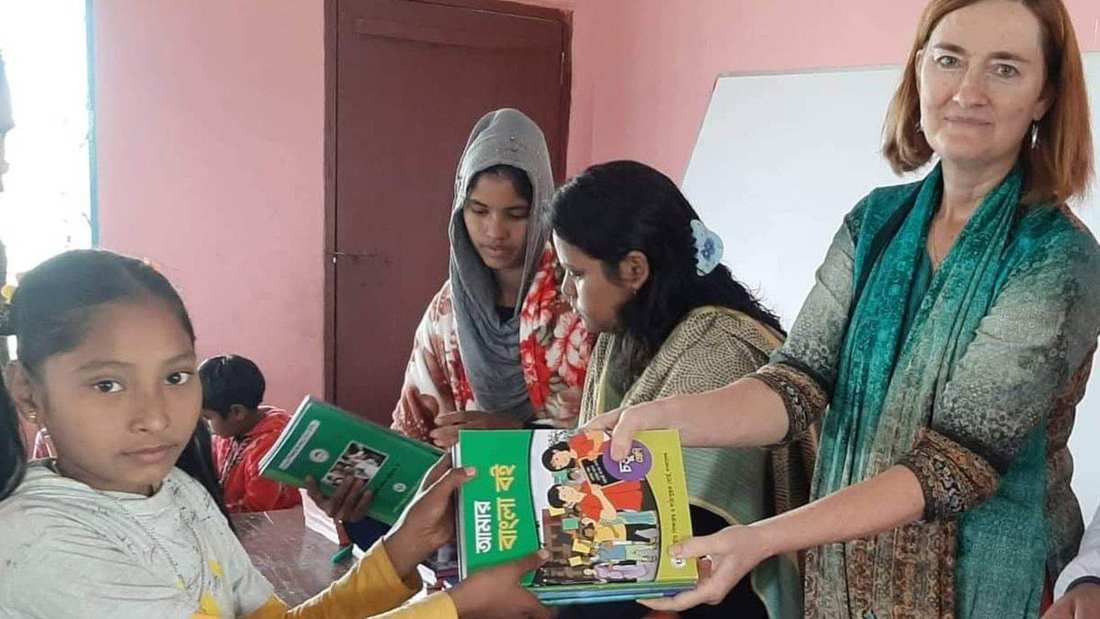 An Oasis for Posterity volunteer hands new schoolbooks to students at a learning session in Jaldhaka, Bangladesh