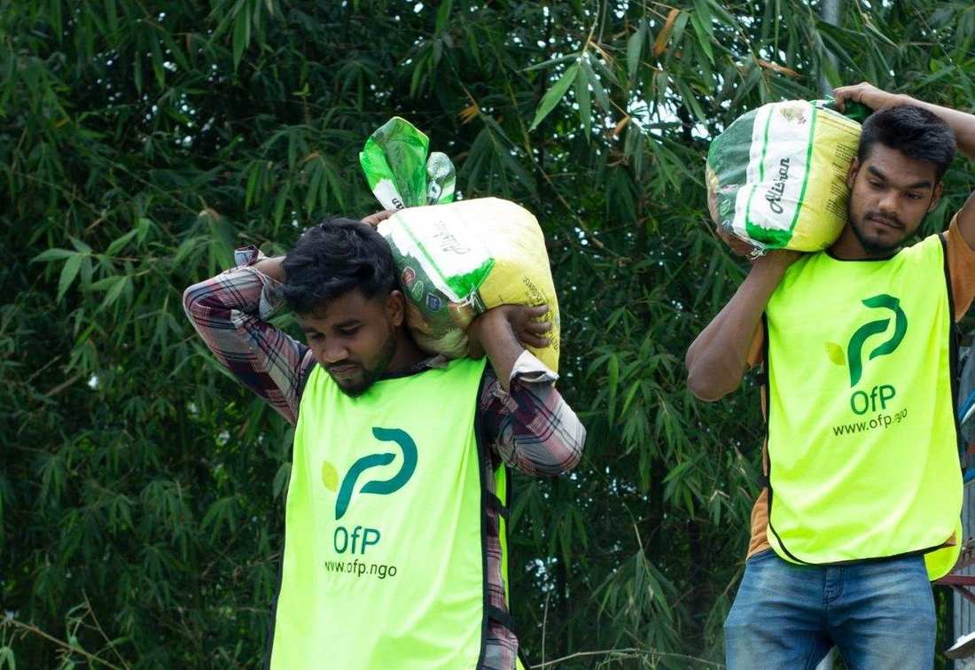 OfP volunteers in branded vests carrying sacks of rice for distribution