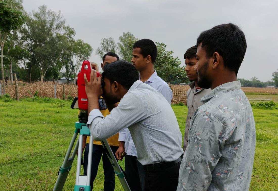 Students learning land surveying with a total station in a field